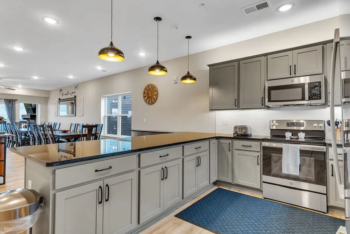 A close-up view of the kitchen island with modern appliances, stylish pendant lights overhead, and bar stools welcoming guests to pull up for a drink or snack. The contemporary design and warm tones create a welcoming atmosphere for cooking and socializing.