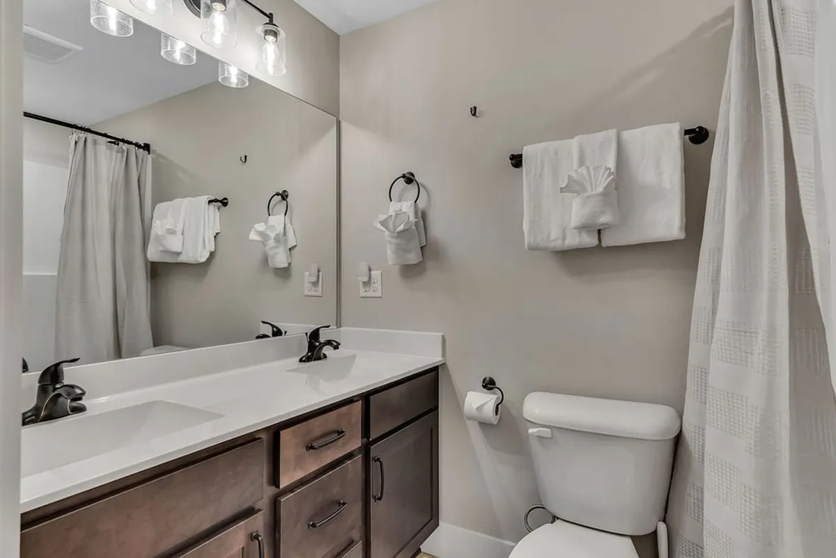 A bright and functional bathroom featuring a double sink vanity, large mirror, and a shower curtain. The space is inviting and practical, ideal for families or groups needing privacy and convenience during their stay.