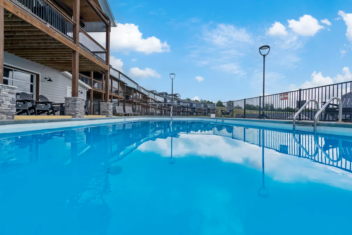 An exterior view of the resort's outdoor swimming pool, complete with a spacious deck, lounge chairs, and a building facade in the background. The mood is cheerful and relaxed, perfect for sunbathing or social gatherings.
