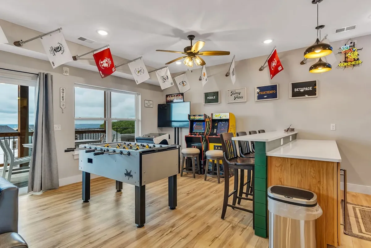 The photo showcases another angle of the game room with the foosball table, arcade machines, and a bar counter. The setting is relaxed and inviting, emphasizing social interaction and playful experiences.