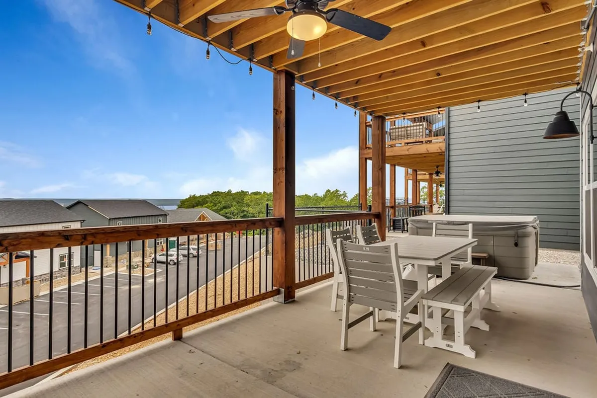 An exterior deck area with a wooden ceiling, outdoor dining set, and a hot tub, framed by lush views and railings. The inviting set-up encourages alfresco dining, morning coffee, or relaxing while soaking in the scenery—perfect for enjoying the private screened-in deck mentioned in the section.