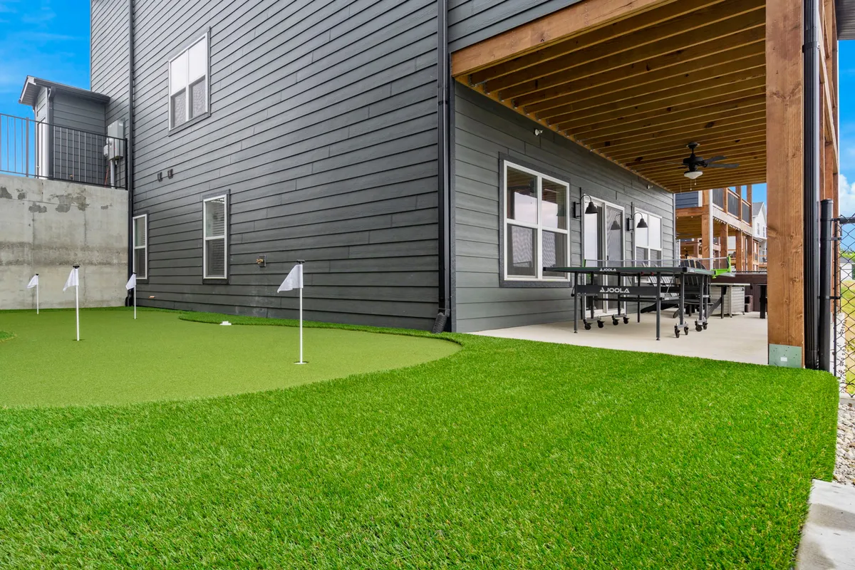 This exterior image highlights the putting green just outside the covered patio, with outdoor dining furniture and a clear view of leisure amenities. The mood is playful and relaxed, ideal for golf practice or casual gatherings.