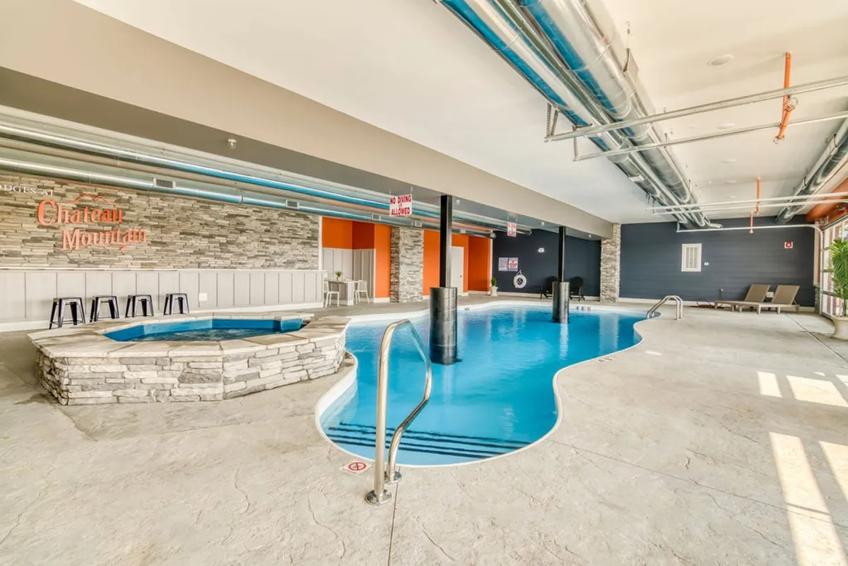 This interior image showcases a tranquil indoor swimming pool with a hot tub, stone wall accents, and a comfortable seating area. The space is well-lit, conveying both relaxation and the inviting atmosphere of a high-quality resort amenity.