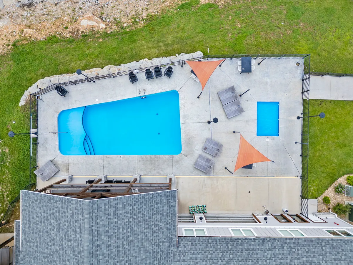 A sparkling outdoor swimming pool flanked by modern lounge chairs and shaded by stylish sails, set against lush grassy surroundings. The setup suggests spaces for sunbathing, swimming, and outdoor socializing.